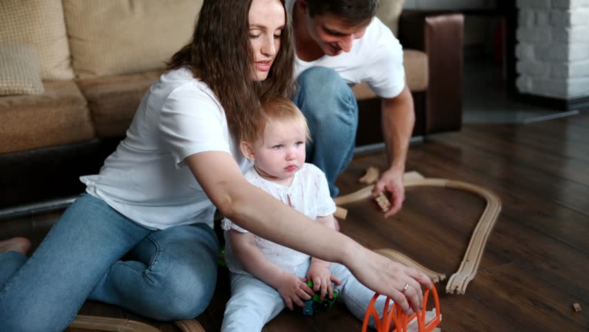 Child sits on floor next to his parents and cries loudly, being capricious until mom and dad give him toy and start building toy road train together. Concept of children's whims, tantrums. 