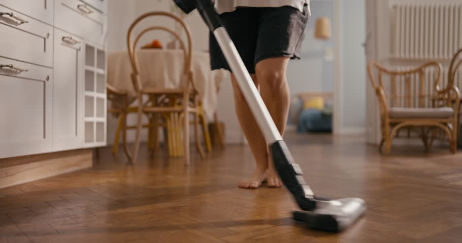 Close-up of a girl in shorts vacuuming and dancing barefoot on the floor at home in a cozy apartment. Cheerful girl cleans and dances at home