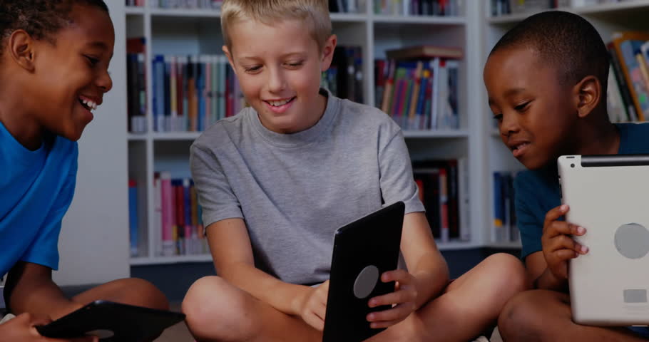 Three boys cross-legged library corner interacting with tablets, exploring financial charts overlay. Technology, education, teamwork, innovation, digital, curiosity, youth