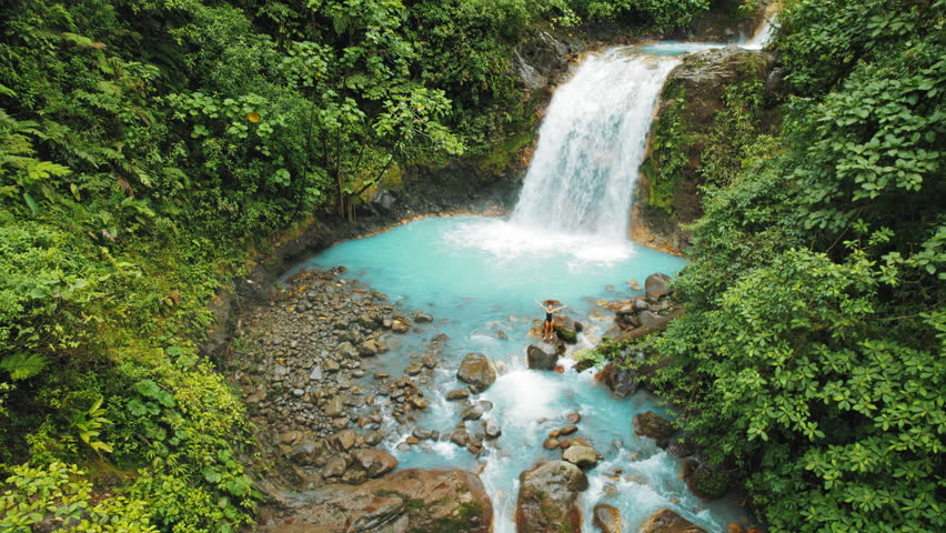 Traveler celebrates on rocks beneath Costa Rica blue jungle waterfall cascade