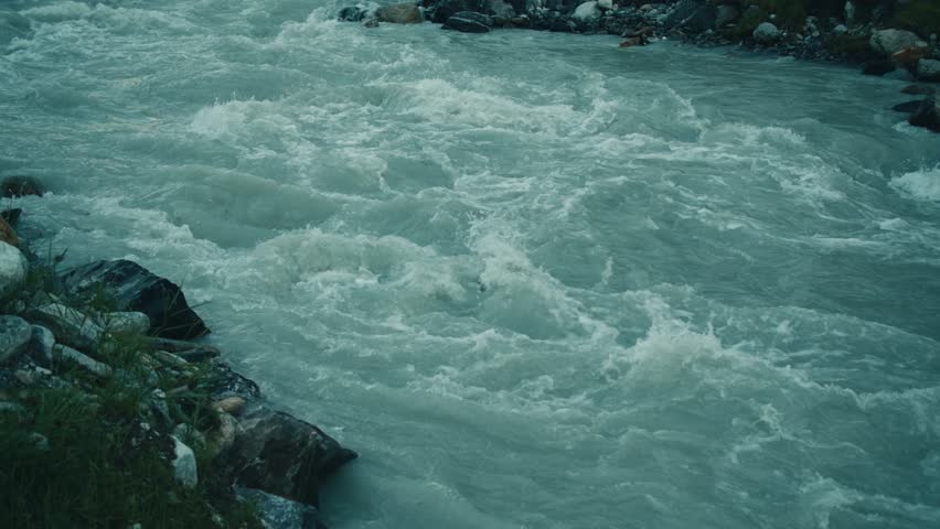 raging fast narrow mountain river in Switzerland slow motion. rapid streams of water waves. natural landscape relief mountains village fields. dark gloomy mood of nature dramatic after sunset evening