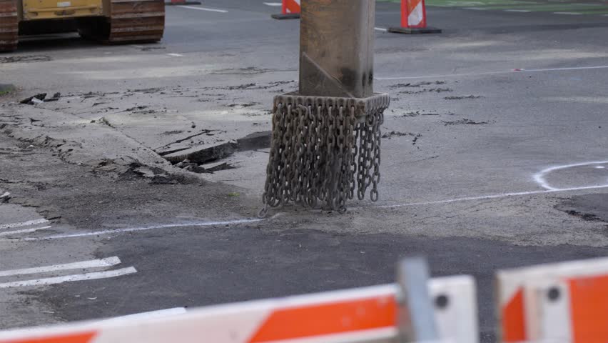 Slow motion of a hydraulic breaker hammer pulverizing asphalt. Chains around the tool swing with impact as chunks of pavement scatter. Powerful industrial equipment. Road construction.