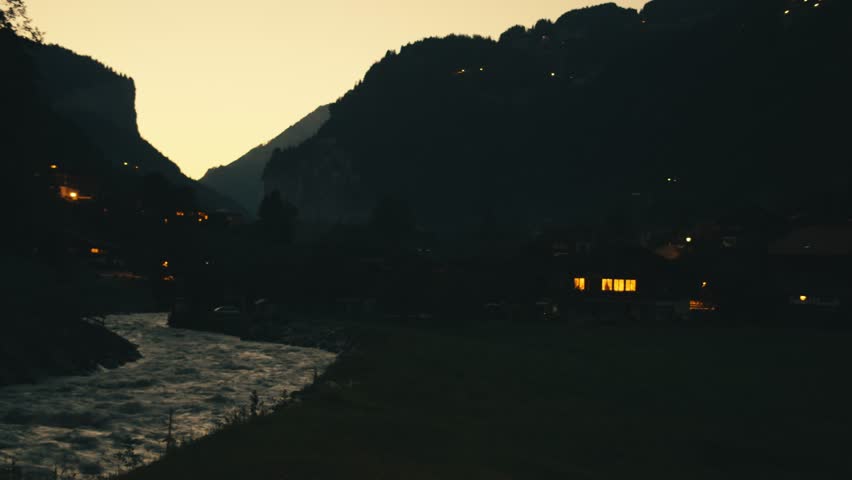 Swiss village at night, lights shining in windows of houses. fast narrow mountain river in Switzerland slow motion. rapid streams of water waves. natural landscape village fields. dark gloomy night