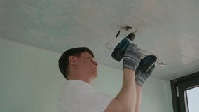 Skilled electrician male in protective gloves installing ceiling light fixture using power screwdriver ensuring secure electrical connections in room. Concept of working with lighting appliances. - Powered by Shutterstock - Get 15% off with code: PIKWIZARD15