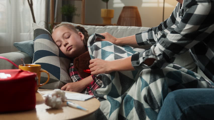Caucasian family at home ill sick sleeping kid girl daughter mother woman mom cover child with blanket touching forehead checking temperature fever childcare health problem medicine symptom pandemic