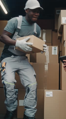 Logistics Retail Warehouse: African American Worker Unloading Cardboard Boxes with Online Orders, E-Commerce Goods. Female Inventory Specialist Using Tablet Computer. Delivery Service. Vertical Shot.