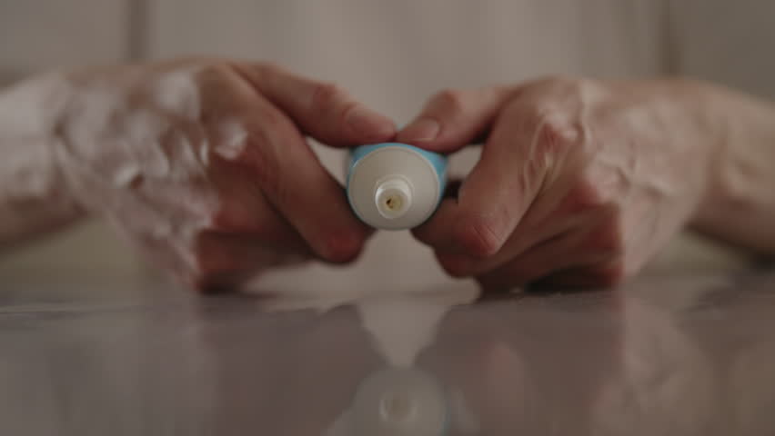 Male hands squeezing moisturizing cream from tube onto table, preparing for skin treatment or cosmetic procedure at home. Concept of beauty and care involved in skincare. Shooting in slow motion.