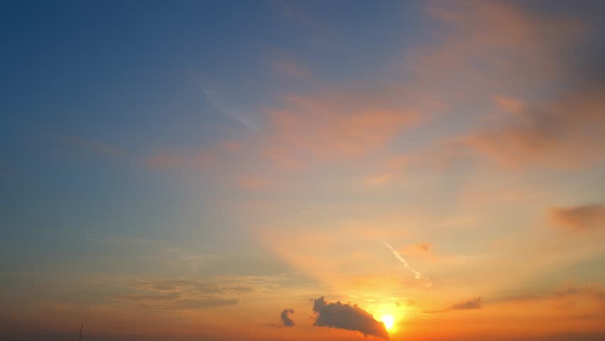 Golden sunrise time-lapse blooms softly across the sky, blending pastel oranges and pinks with calm blue. Clouds drift gently, glowing warmly as dawn’s light awakens a new day’s promise. Timelapse.
