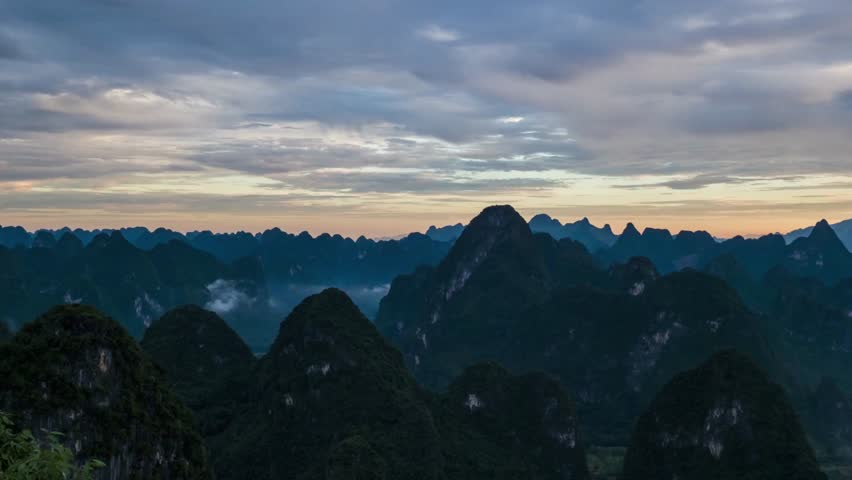 Karst mountains stretch across the horizon under a cloudy sunset sky