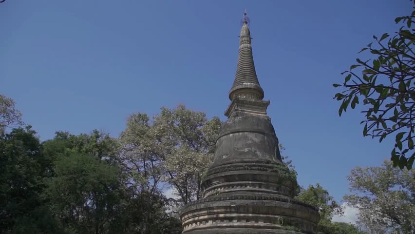 Ancient buddhist pagoda rises among the trees against a clear blue sky