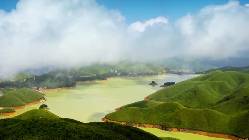 Green hills surround a serene lake under a cloudy sky in a scenic landscape