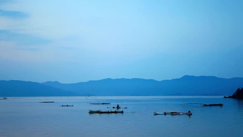 Tranquil lake reflects mountains and sky at dusk with boats on the water