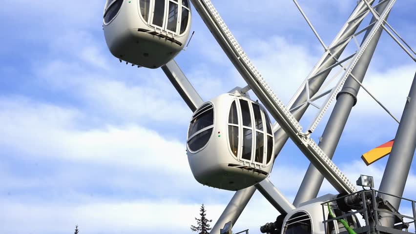 Ferris wheel cabins rise up against blue sky at amusement park