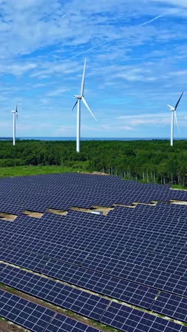 Aerial parallax shot showing a large solar farm with photovoltaic panels and wind turbines generating clean, renewable electricity in a beautiful green landscape in Latvia.