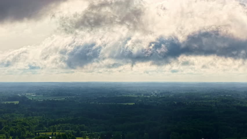 Dramatic cloud formations over vast green landscape under daylight sky