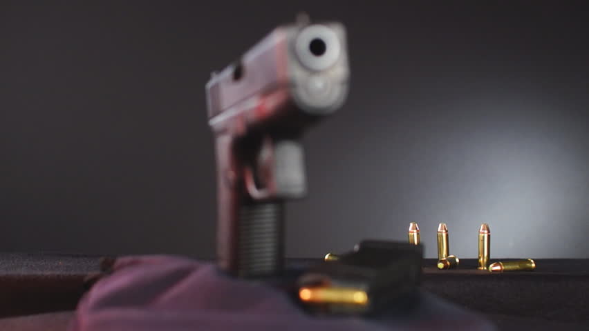 Semi-automatic pistol rotating with bullets in background.