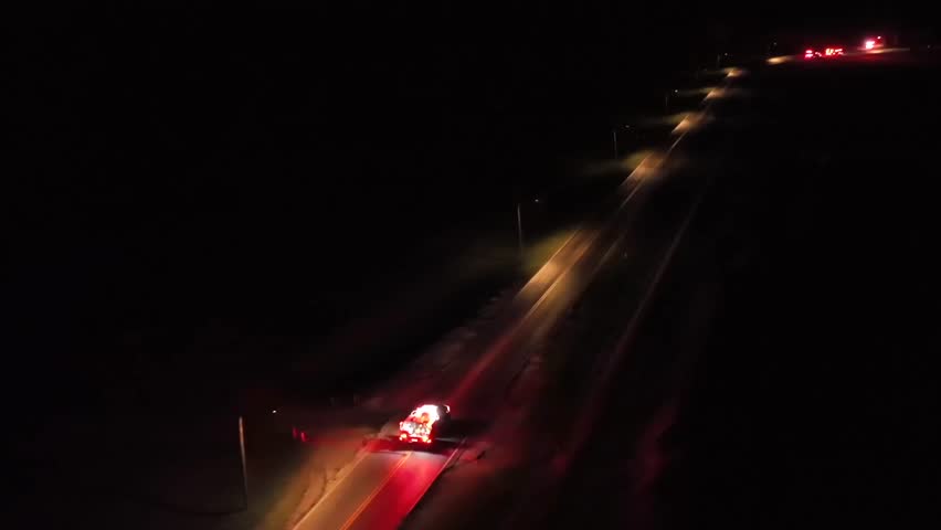 Emergency vehicle and fire truck on illuminated suburb intersection in America. Burning bush fire in forest. Aerial tracking shot. Night scene.