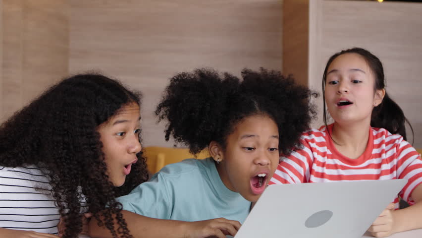 Multicultural girl students feel excited and happy together, sitting at a table and learning with a laptop.