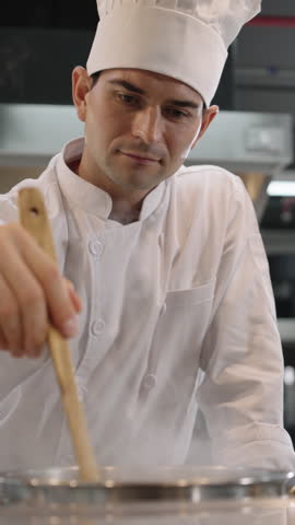 Male chef prepares wearing uniform stirring food in professional restaurant kitchen with focus and passion, showing professional cooking skills.