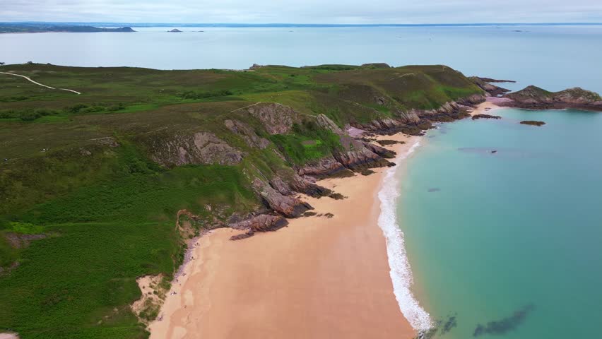 The idyllic Plage de Lourtuais beach, the rocky peninsula of Cap d'Erquy, and calm turquoise sea in Brittany, France. Aerial drone lateral