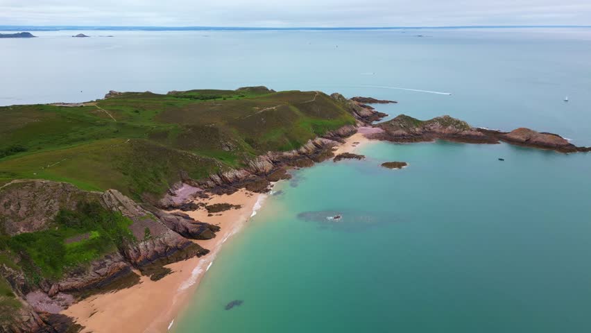 Aerial backward drone view of the idyllic Plage de Lourtuais beach, the rocky peninsula of Cap d'Erquy, and calm turquoise sea in Brittany, France