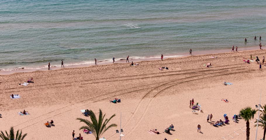 Slow motion aerial footage of the lively Spanish city of Benidorm showing the Playa de Levante beach with local people and tourists on vacation relaxing sunbathing enjoying the sandy beach
