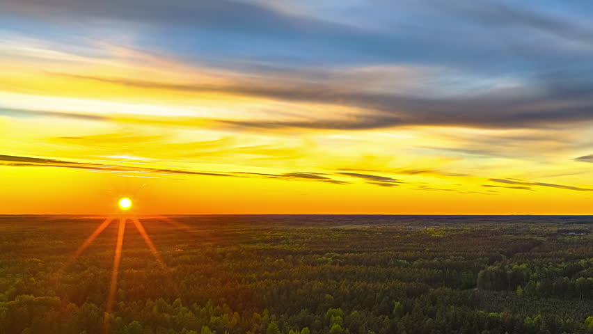 Golden sunset as the sun disappears beyond the forest horizon - high altitude, colorful aerial time lapse