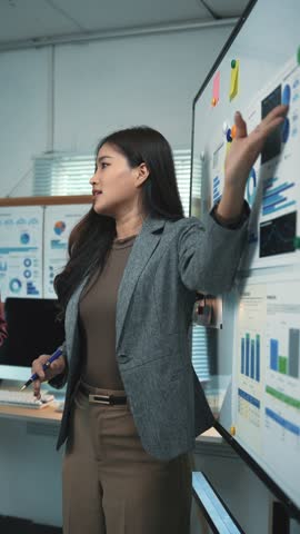 Professional businesswoman analyzing marketing data, presenting strategic insights on whiteboard while collaborating with colleagues in corporate office setting