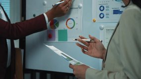 Businesswoman pointing at charts and graphs on whiteboard, presenting loan comparison to businessman in office meeting - Powered by Shutterstock - Get 15% off with code: PIKWIZARD15