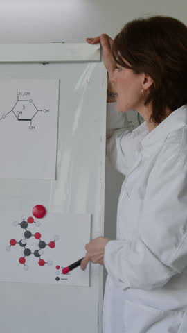 Vertical shot of female science teacher delivering lecture, using white board and illustrations during chemistry class in laboratory