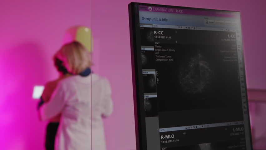 A woman undergoing a mammogram with a medical professional present, displaying the process on a screen. Woman Undergoing Mammogram