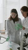 Vertical shot of female science teacher in lab coat and protective glasses conducting test tube experiment wit her student in laboratory - Powered by Shutterstock - Get 15% off with code: PIKWIZARD15