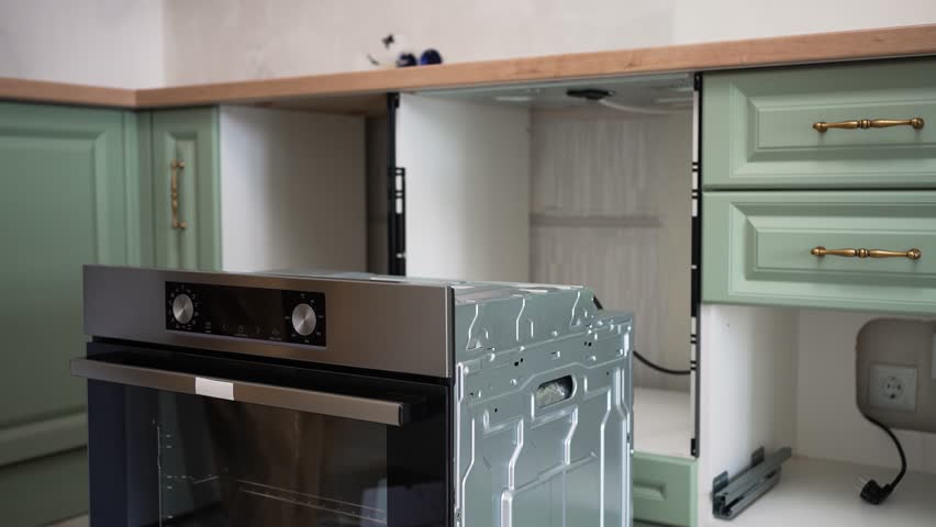 Furniture assembly worker carefully installs a new oven in a kitchen cabinet, connecting it and ensuring proper placement and functionality