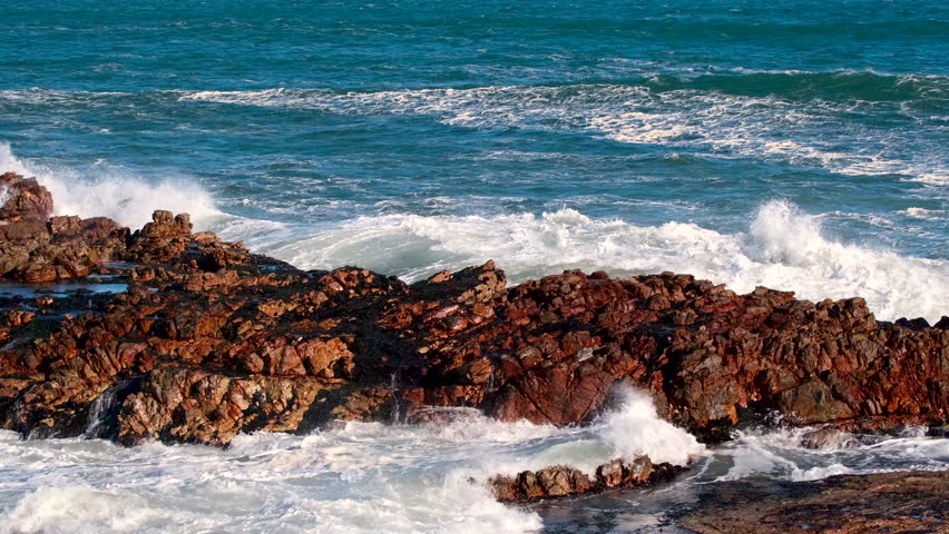 Atlantic wave crashes dramatically over coastal rocks in slow motion, telephoto