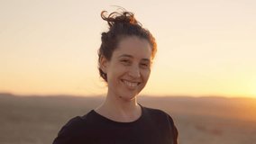 Female traveler or hiker smiling looking at camera on windy desert day at sunset. Beautiful natural landscape outdoors. Wind blowing woman's hair as she enjoys being outside. Close up portrait - Powered by Shutterstock - Get 15% off with code: PIKWIZARD15