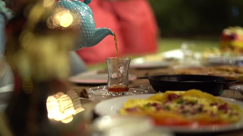 A man pours tea on a cup around Egyptian breakfast, close up shot, high angle shot, insert shot