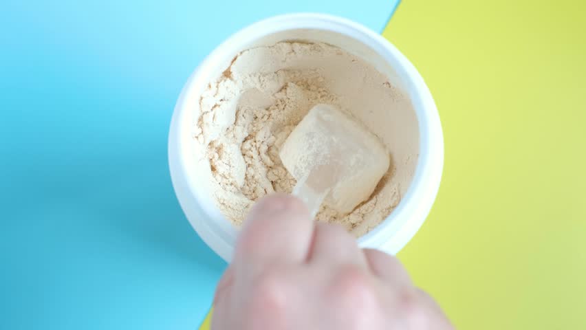 Protein powder in scoop and plastic jar on blue and yellow background.