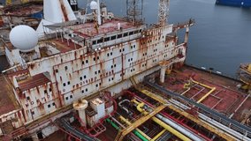 Aerial drone view of an old red tanker with a heavily rusted superstructure. The aging vessel is docked and prepared for dismantling into scrap metal at an industrial shipbreaking yard. - Powered by Shutterstock - Get 15% off with code: PIKWIZARD15