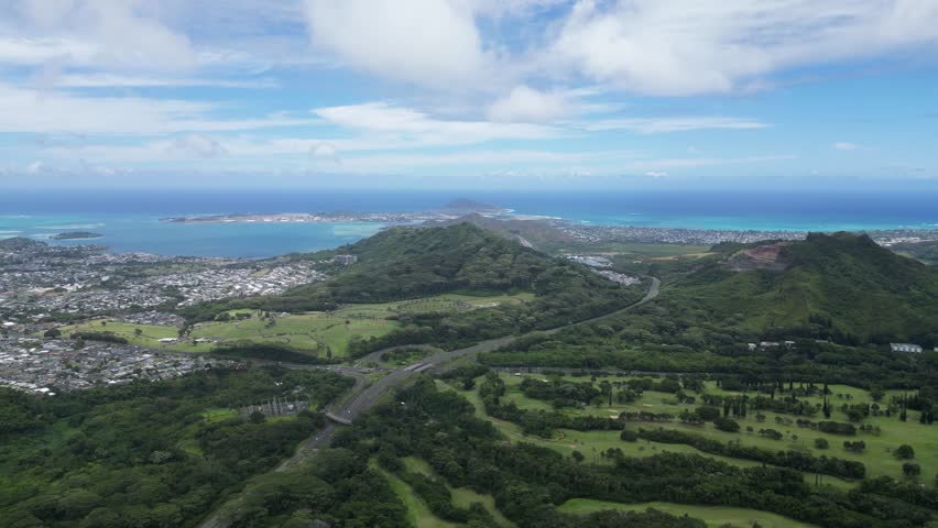 Drone footage showing a panoramic view of Hawaii’s coastline, green mountains, urban areas and cloudy sky.