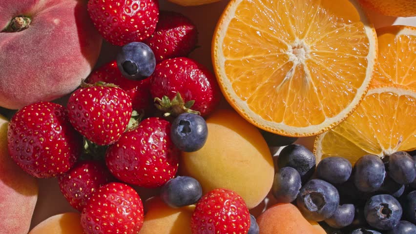 closeup of various rotating fresh bright summer fruits and berries, top view. healthy sunny food background 