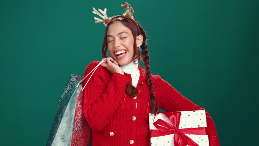 Christmas, face and happy woman with shopping bags in studio for celebration, dance or laugh. Xmas, portrait and excited shopaholic with gifts, holiday presents or box for fashion on green background