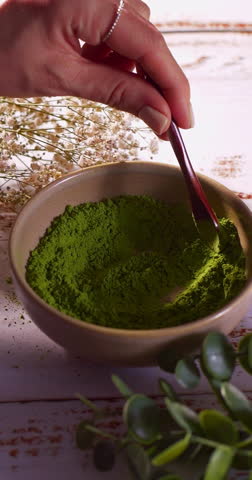 Close up slowmotion of wooden spoon gently stirring vibrant green powder in ceramic bowl. content related to tea, wellness, superfoods in a natural setting. Matcha , Barely gras, Vitamin or Spirulina.