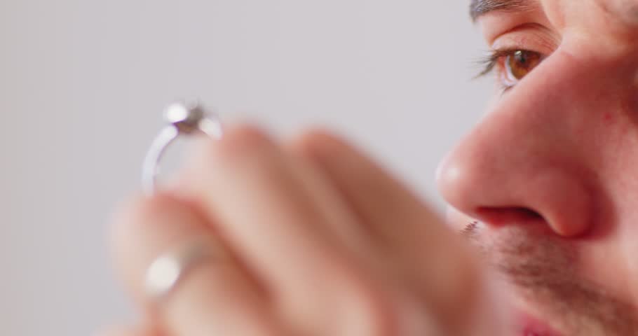 Closeup portrait of male jewellery appraiser inspecting gold ring with diamond looking through magnifying glass isolated on white background. Man jeweler and goldsmith evaluating jewelry. 4k video.