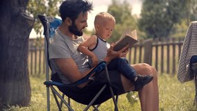 Father and son enjoying quality time outdoors, sitting on a camping chair in a sunny backyard. Dad is reading a book to his curious toddler. Warm family moment, nature, parenting, bonding concept - Powered by Shutterstock - Get 15% off with code: PIKWIZARD15