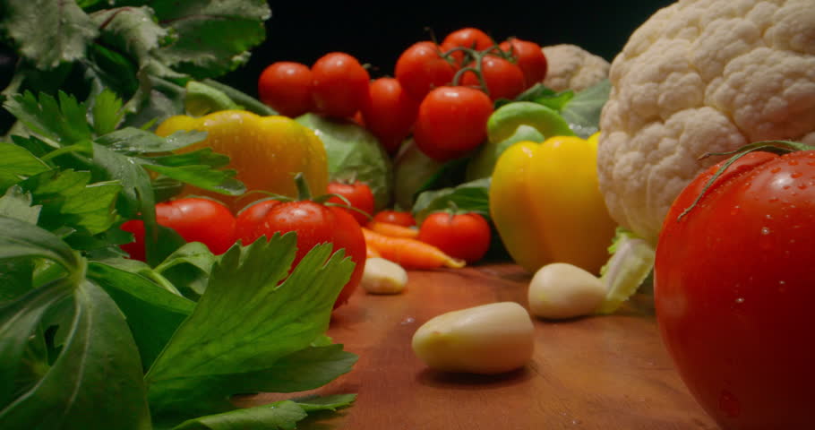 Assortment of fresh vegetables including tomatoes cauliflower bell pepper carrots garlic cloves cabbage leafy greens on black background. Diet healthy nutrition vitamins