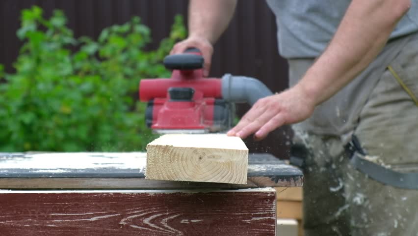 Male carpenter using electric circular saw in backyard workshop with wood chips flying. Building contractor worker cutting plank by fretsaw tool to cut boards on new home construction project. Sawing