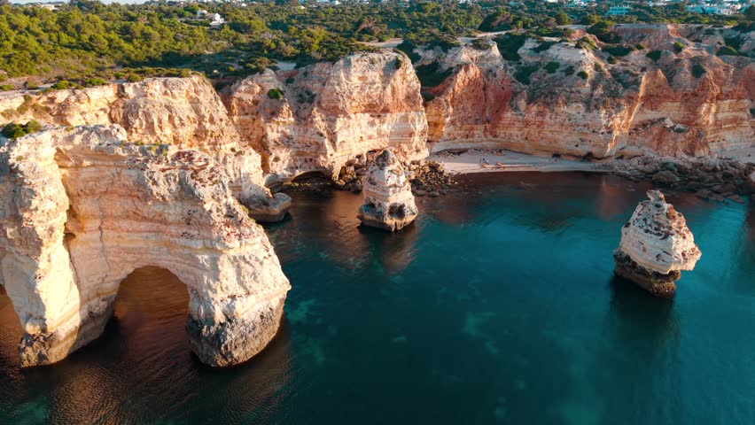 Breathtaking aerial view showcasing the striking coastal cliffs and crystal-clear waters of the Algarve region in Portugal, highlighting natural beauty and tranquility.