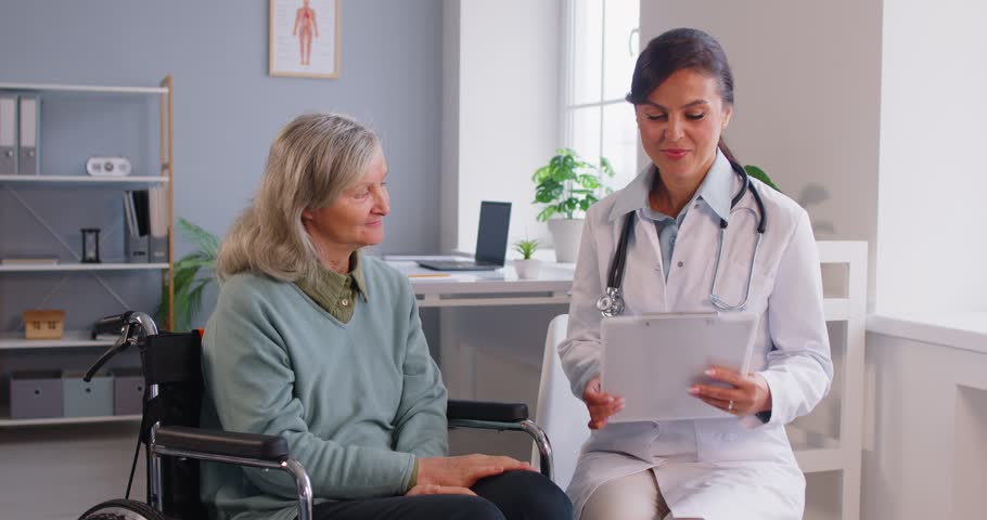 Geriatric medicine doctor in clinic, nurse, geriatrician physician talking to disabled old senior sitting in wheelchair, supports handicapped patient, medical rehabilitation, assistant or caregiver