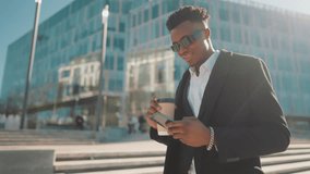 Walk in city in morning, black man strolling with cup of coffee in downtown. Portrait of self-confident young adult african male person enjoying sunny weather and good mood, modern people in city - Powered by Shutterstock - Get 15% off with code: PIKWIZARD15