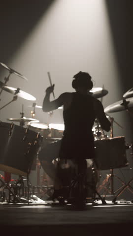 Man playing drum set alone in dark rehearsal room or stage, back view of male musician enjoying music and rhythm. Silhouette of brawny cool guy beating cymbals and drums, rear view in soffit light